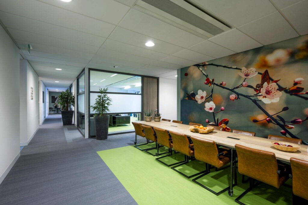 Moderne kantoorruimte aan de Laan van de Helende Meesters met een lange vergadertafel, lederen stoelen en een grote muurprint van bloesemtakken.